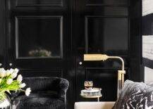 Contemporary living room features a glossy black wall trim with black velvet chair and a cream sofa with black and white pillows lit by a brass floor lamp.