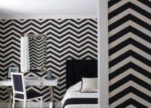 Contemporary black and white bedroom features black and white chevron wallpaper, a black and white French bed, a chrome x base desk as nightstand under a studded mirror with a black and white French chair and a black, white and gray rug.