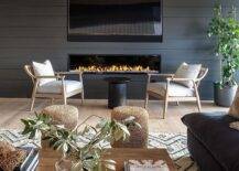 Living room features a black shiplap fireplace under a flatscreen TV, beige vintage accent chairs with a black pedestal accent table and woven stools at a wooden coffee table.