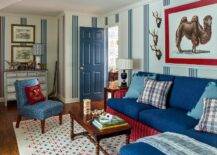 Living room features a red and blue skirted sofa with vintage spindle coffee table atop a red and blue rug, a blue accent chair and a blue door.