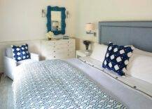 Bedroom features a blue coral mirror over a tall white dresser, a blue headboard with blue trellis pillows and a light blue accent chair.