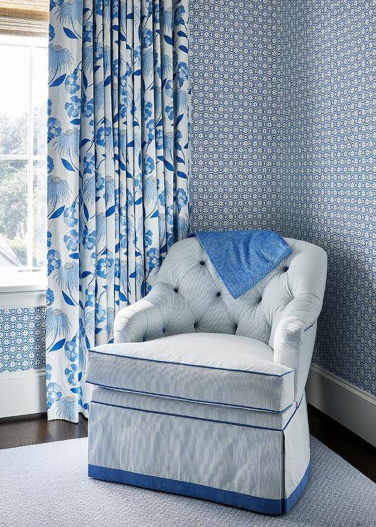 Bedroom features a blue pinstripe tufted chair with skirt, blue and white wallpaper and a blue and white curtain.