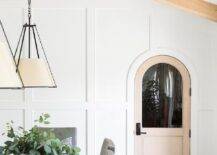 Cottage dining space designed with board and batten trim, an arched door and beams on a vaulted ceiling.