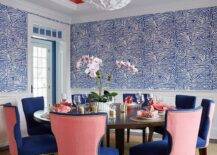 A glossy pink gray ceiling complements a round brown wooden dining table paired with blue and pink dining chairs placed on a natural woven rug. Wainscot walls are finished with Brunschwig & Fils Ashanti Wallpaper.