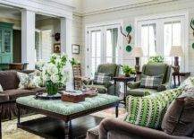 Brown and green living room features a green tufted ottoman coffee table placed on a gren rug between facing brown velvet sofas accented with green, brown, and blue pillows. Green leather club chairs sit side-by-side topped with green plaid pillows.