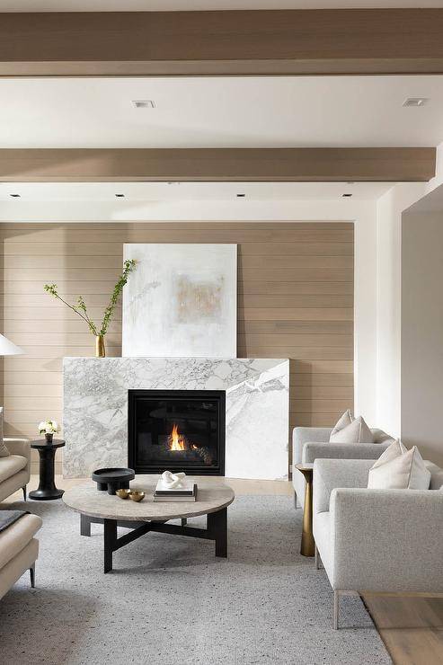 A white and brown abstract art piece sits on a marble beveled fireplace mantel against a light brown plank wall.