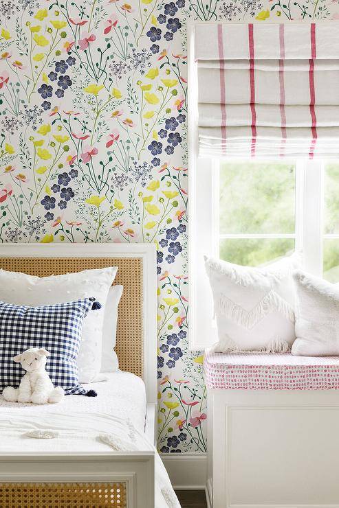 Bedroom features a cane headboard with gingham pillow on floral wallpaper and a red and white window shade.