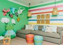 Contemporary family room features a gray sectional on a striped accent wall lit by basket lanterns, red and blue woven stools, and colorful paper mache animal heads on a green wall.