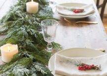 a cozy and homey winter table with an evergreen and pilalr candle runner, berries and evergreens plus gold cutlery