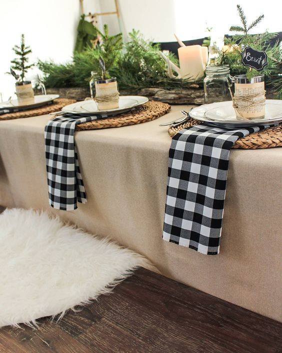 a cozy rustic winter table setting with plaid napkisn, woven placemats, evergreens, candles and antlers and jars with candles