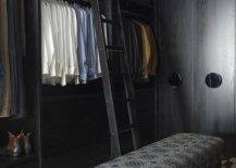 Modern black oak custom walk in closet with a black ladder on rails features cubbies with black woven baskets and a black and silver bench on black and white flooring.