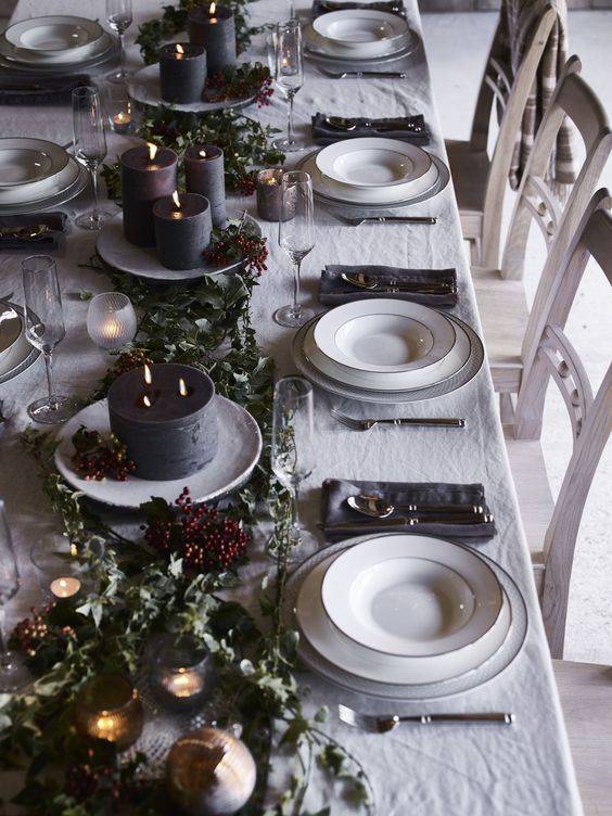 a chic dark tone winter tablescape with dark candles, greenery, berries, grey napkins and white porcelain