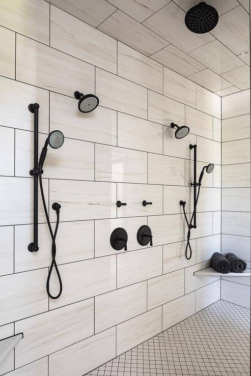 White lattice floor tiles accent a walk-in shower fitted with his and hers oil rubbed bronze shower kits mounted to large white offset wall tiles, a bronze rain shower head, and a corner floating bench.