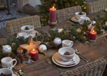 a chic winter table setting with an evergreen, lights and pinecones runner plus wooden stars and ornaments, pillar candles and pinecones in bowls