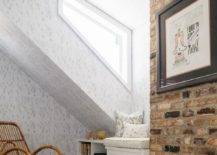 Gender neutral attic nursery features a red brick wall, rattan nursery rocker and a built-in window seat with whimsical pillow.