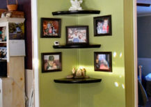 Green wall with corner-mounted floating shelves holding pictures, stones, and small sculptures.