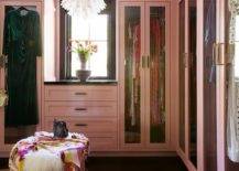 Glam pink walk in closet boasts pink built-in wardrobe cabinets over a gold metallic cowhide rug atop black floor tiles and a round accent table.