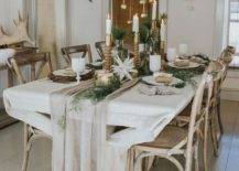 a chic and neutral winter tablescape with a neutral runner, greenery, paper stars candles in various candleholders and ornaments hanging over the table