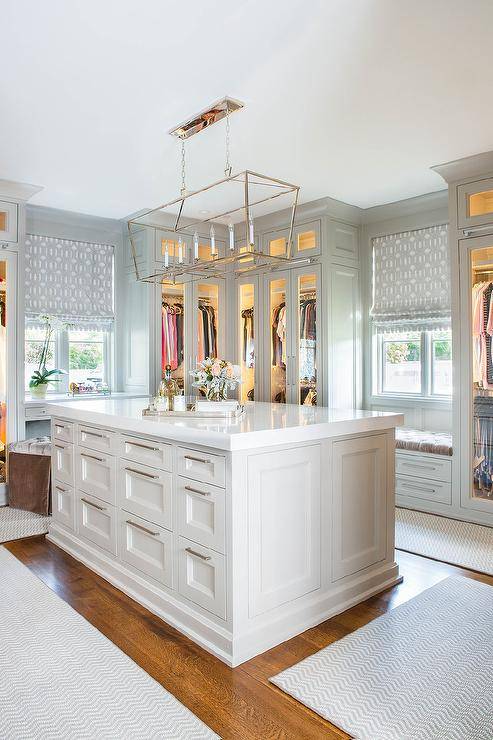 Darlana Linear Chandelier illuminates above a custom walk-in closet rectangular island surrounded by custom built-ins and a window seat.