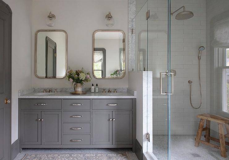 A gray wooden dual bath vanity dons polished nickel hardware and a gray marble countertop holding polished nickel cross handle faucets under curved nickel mirrors lit by nickel and glass sconces.