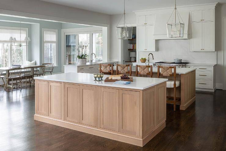 White and tan kitchen features dual tan wooden island, with one island matched with wood and abaca counter stools and nickel lanterns.