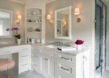 A pink faux fur stools sits at a white built-in makeup vanity accented with a gray and white marble countertop and polished nickel pulls. Above the vanity a white mirror is lit by Camille Long Sconces, while styled shelves are mounted in the corner. On an adjacent wall, a white washstand is finished with a polished nickel faucet kit fixed to a gray and white marble countertop beneath a white mirror flanked by Camille Long Sconces.