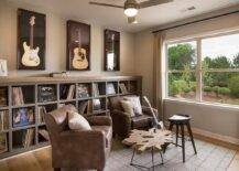 Man cave and music room combo features a row of guitars framed in shadow boxes placed over an industrial shelving unit filled with vintage vinyl records. Industrial man cave room boasts a pair of brown leather club chairs facing a driftwood coffee table placed in front of windows dressed in beige curtains.