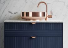 Bathroom with marble walls, blue vanity, and copper sink and fixtures.