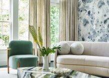 Contemporary living room features a green, black and gray lacquered coffee table with a gold and green chair, cream sofa and black and white accent wall.