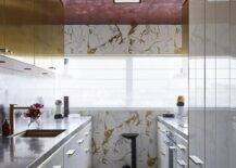 Contemporary kitchen features white and gold lacquer cabinets with black marble top and a red ceiling.