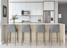 A brown veneer peninsula is complemented with modern gray leather stools and finsiehd with a sink with a satin nickel gooseneck faucet.