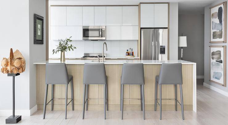 A brown veneer peninsula is complemented with modern gray leather stools and finsiehd with a sink with a satin nickel gooseneck faucet.