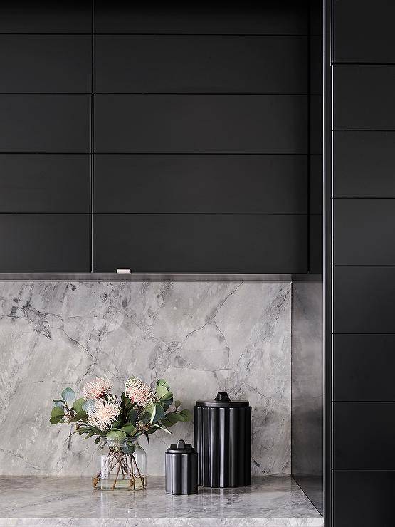 Modern gray and black kitchen features black plank cabinets with a gray marble slab backsplash.