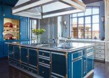 Spacious kitchen features a peacock blue metal island with stainless steel countertop and dual gas cooktops and blue cabinets.