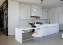 Spacious modern white kitchen features white velvet and acrylic stools at kitchen island dining table, an island sink with copper faucets and white flat front cabinets.