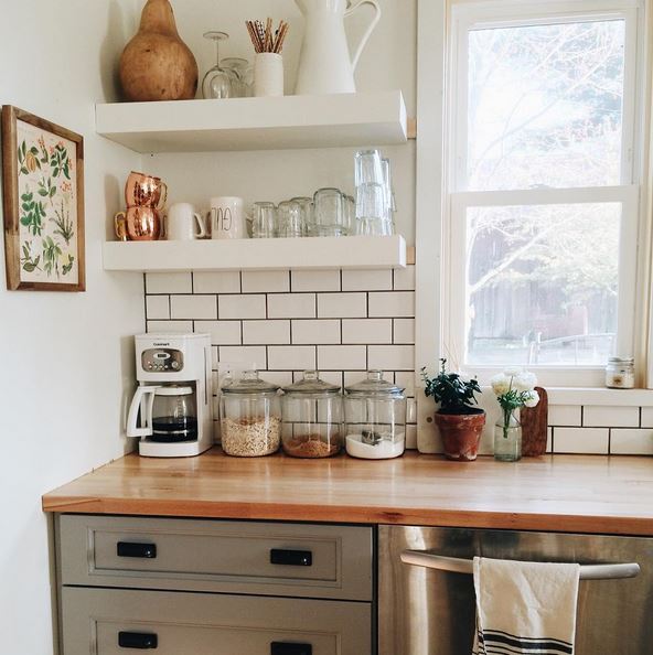 Minimalist kitchen that has floating white shelves to hold mugs, cups, and wine glasses.