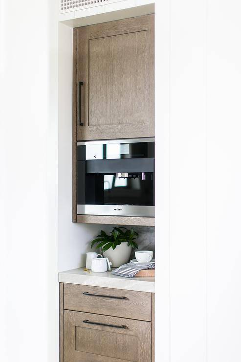 Miele Coffee machine built-in a kitchen nook coffee station between brown oak cabinets with oil rubbed bronze pulls and a light gray quartz countertop.