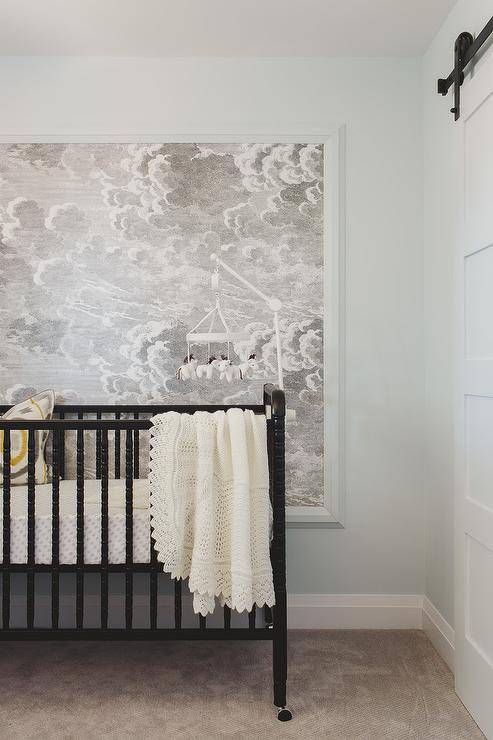 Modern boy's nursery features a horse mobile over a black nursery crib against a wall clad in Fornasetti Nuvole framed cloud wallpaper.