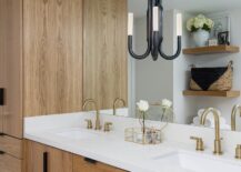 Bathroom features a Kelly Wearstler Rousseau double wall sconce on a vanity mirror over a wooden washstand with white countertop and dual brass faucets.