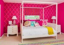 A colorful striped rug covers carpeted floors in this playful teenage girls' bedroom while positioned under a window finished with a purple and red striped roman shade framed by an accented wall covered in Pompeian wallpaper from Cole and Son's , a white canopy daybed dressed in white bedding is topped with pink and turquoise otomi pillows, an assortment of pink and accented pillows, and a mustard yellow throw. Flanking the bed are two Bungalow 5 Jacqui 3 drawer side tables topped with pink glass lamps lighting red side walls.