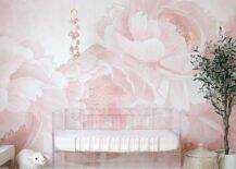 Nursery features a clear crib on a pink floral wall and a tall potted plant.