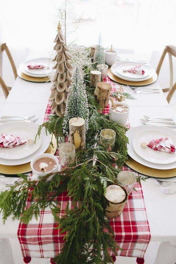 a bright winter table with a red plaid runner, napkins, birch branches, faux Christmas trees and an evergreen runner