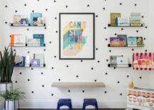 Blue tolix stools at a floating kids desk mounted on a white wall with black triangle decals creating a fun accent wall for black metal wall shelves displaying kids' books.