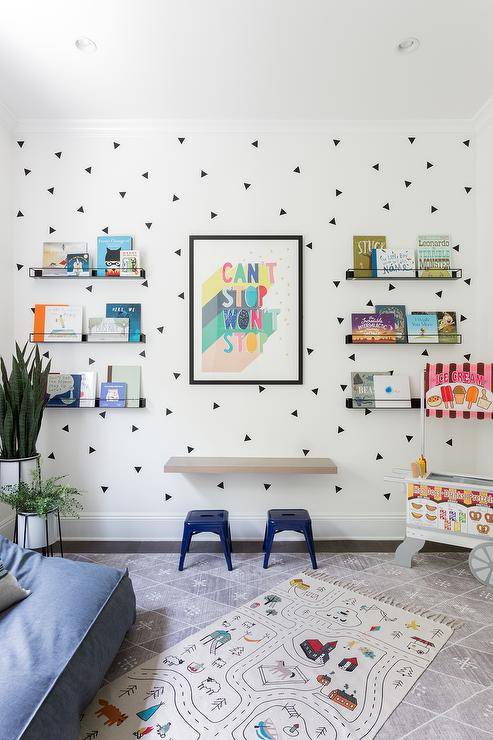 Blue tolix stools at a floating kids desk mounted on a white wall with black triangle decals creating a fun accent wall for black metal wall shelves displaying kids' books.