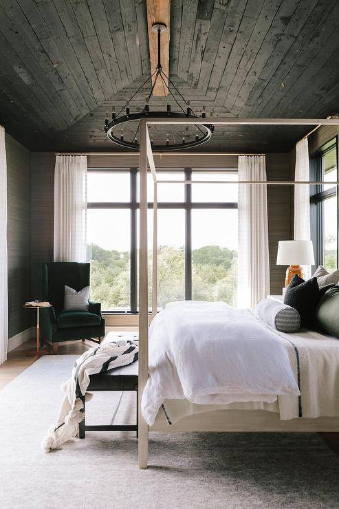 Black oak plank vaulted ceiling above a bedroom showcasing a black round chandelier with a light gray wooden canopy bed and a black bench at the foot.