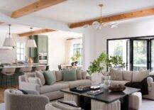 Livng room features a pebble gray couch accented with sage green pillows, a square wooden coffee table with cream boucle stools and gray boucle swivel chairs.