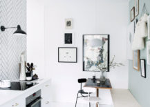 A kitchen with white walls adorned with a black and white chevron pattern. Two chairs are placed in the room, one white and the other is black.