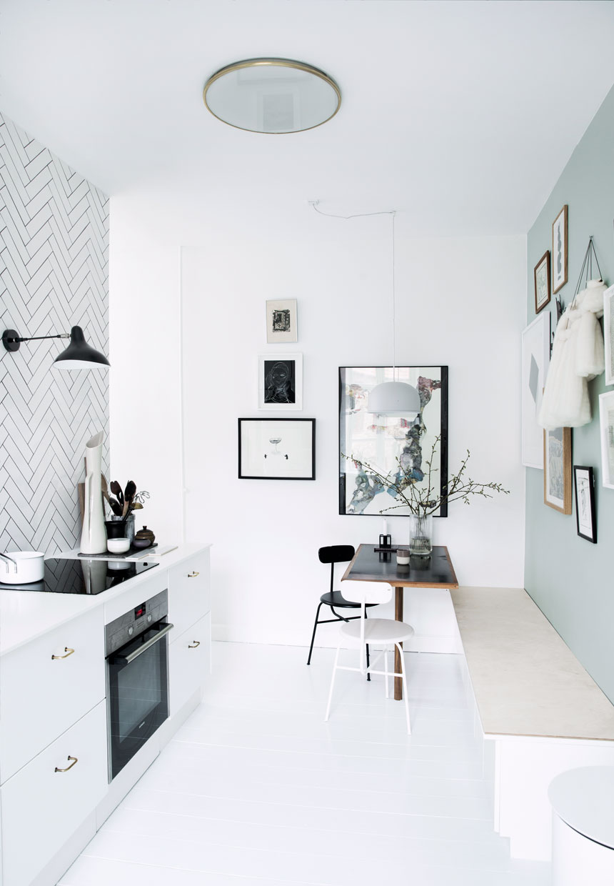 A kitchen with white walls adorned with a black and white chevron pattern. Two chairs are placed in the room, one white and the other is black.