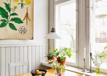 A wooden table with two chairs arranged around it sits in front of a large window. The table is set with a vase of flowers.