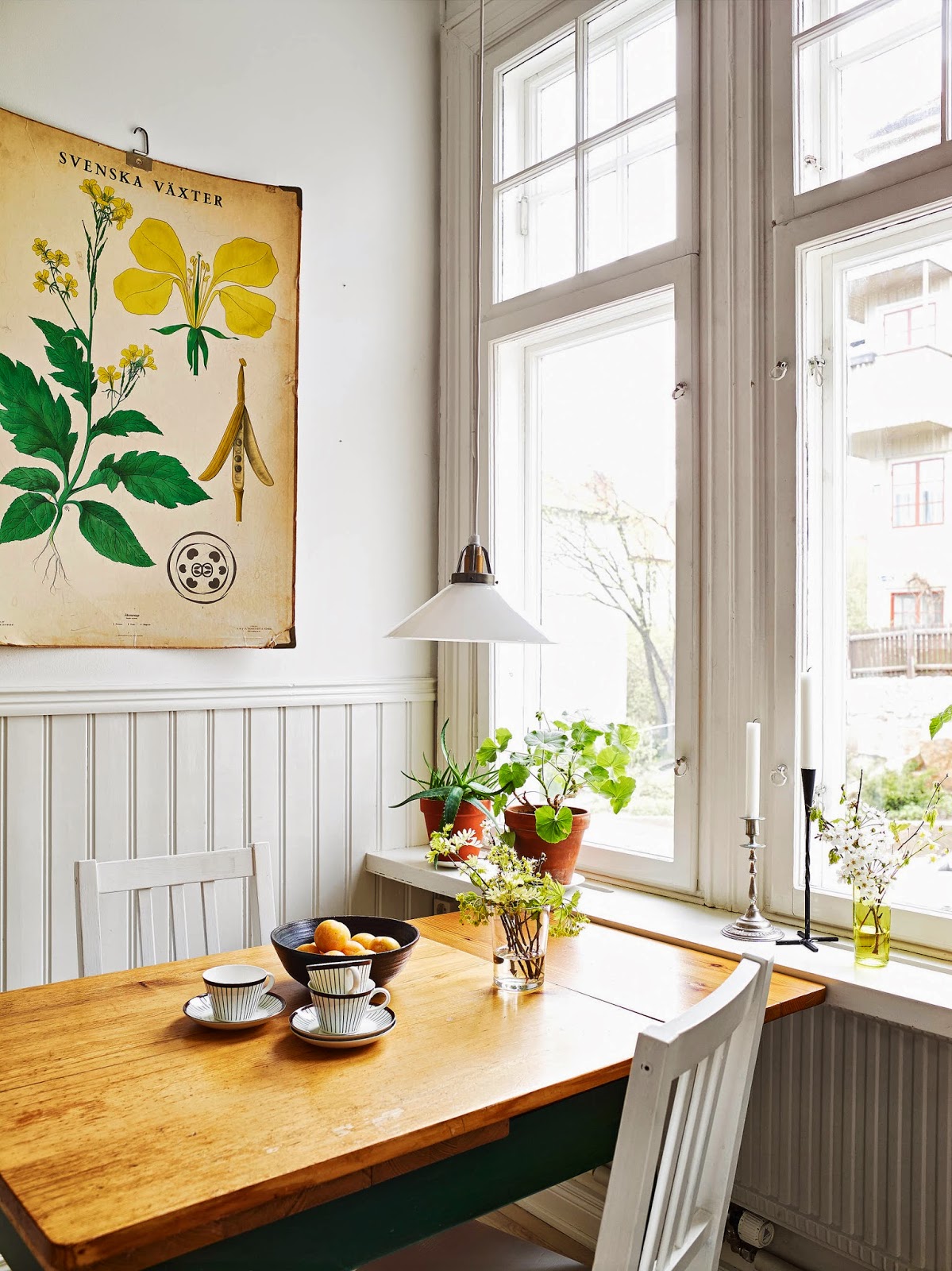 A wooden table with two chairs arranged around it sits in front of a large window. The table is set with a vase of flowers.